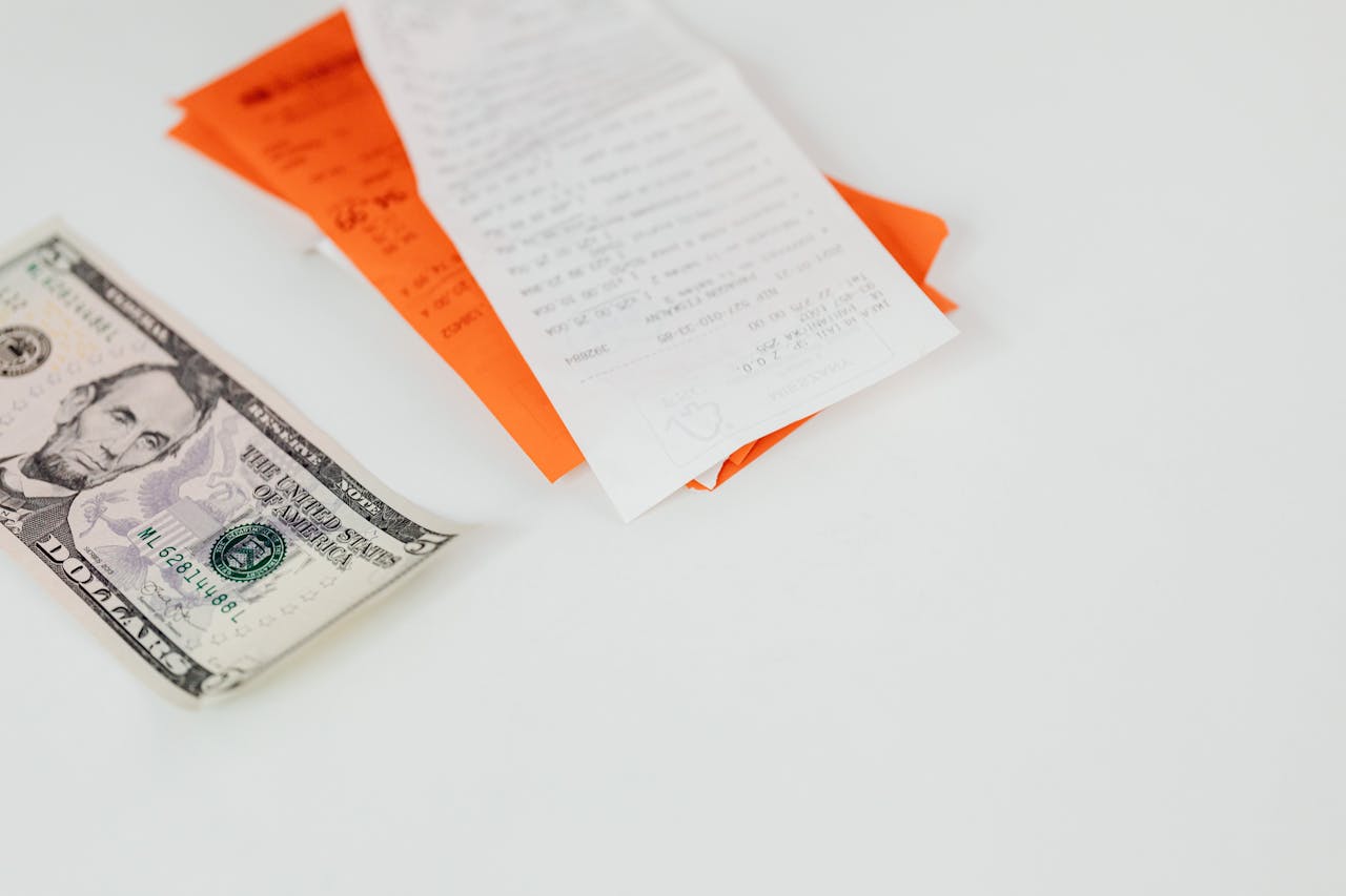 A five dollar bill and receipts on a white surface, emphasizing finance and expenses.